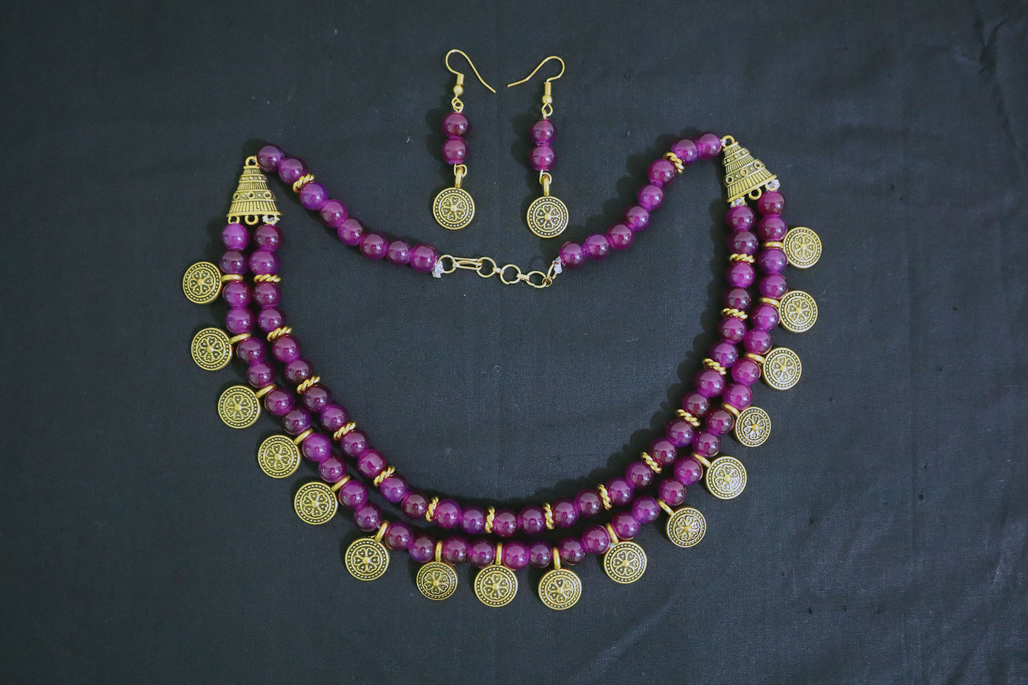Top view of amethyst glass beads and golden ginni necklace with earrings on black fabric