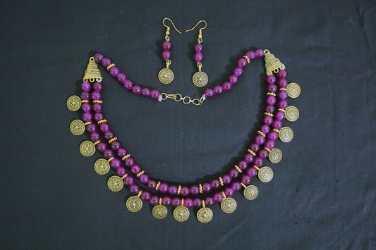 Top view of amethyst glass beads and golden ginni necklace with earrings on black fabric
