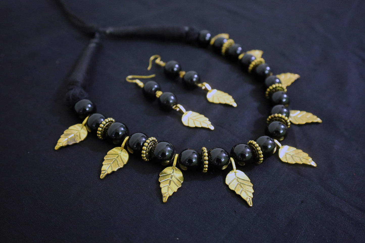 Angle view of handmade black beads and golden leaf charm doughnut necklace with earrings.