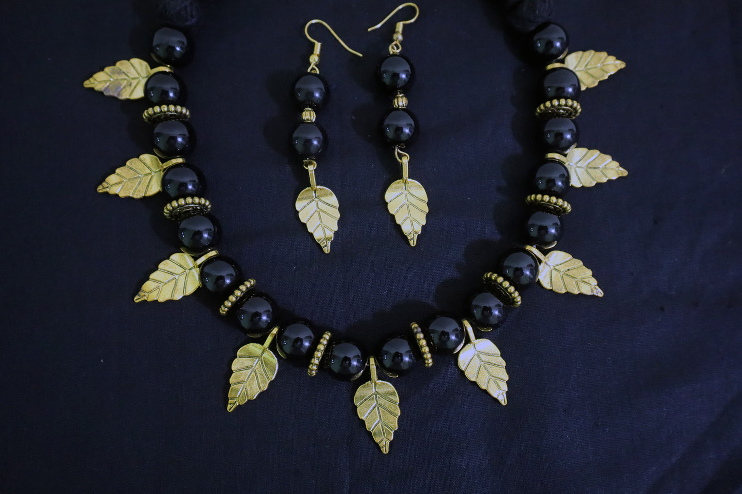 Bottom close-up of big black glass beads necklace and earrings with golden leaf and doughnut design.