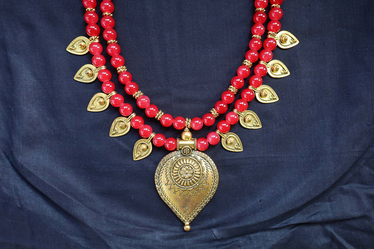 Bottom close-up of red glass beads necklace and earrings with golden drop charm pendant.