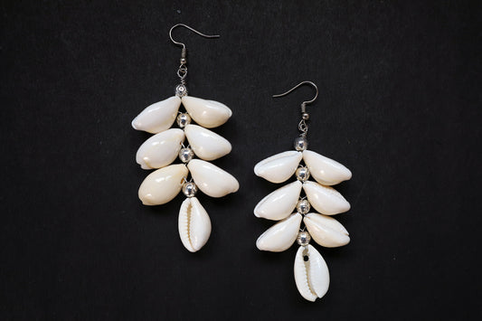 Top view of pair of Cowrie Seashell & Metal Ball Dangle Earrings on black fabric background
