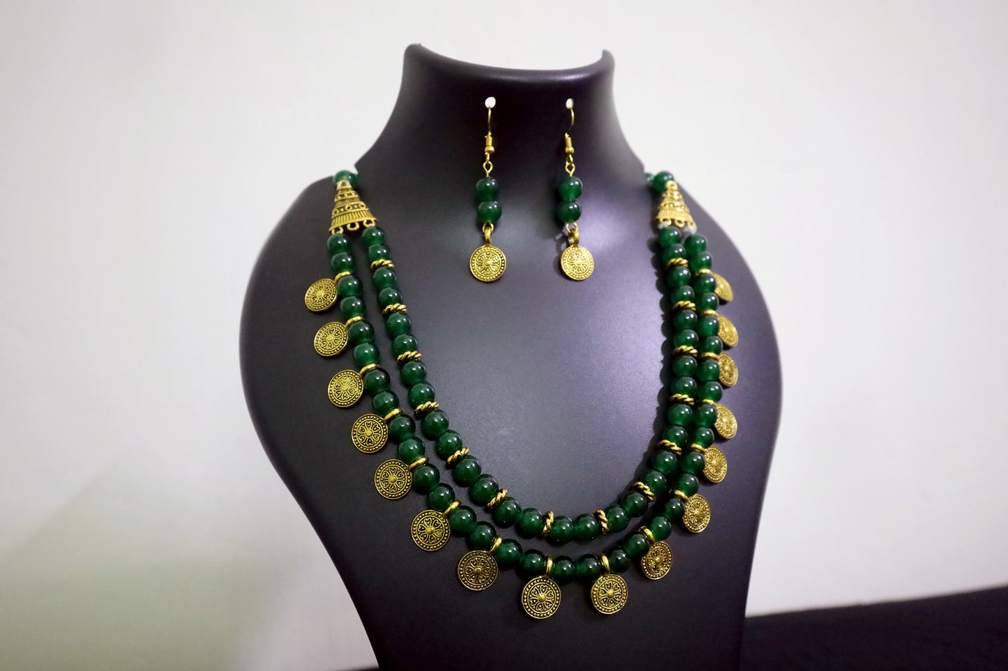 Closer view of dark green 2 layered glass beads golden ginni necklace set with earrings on black mannequin