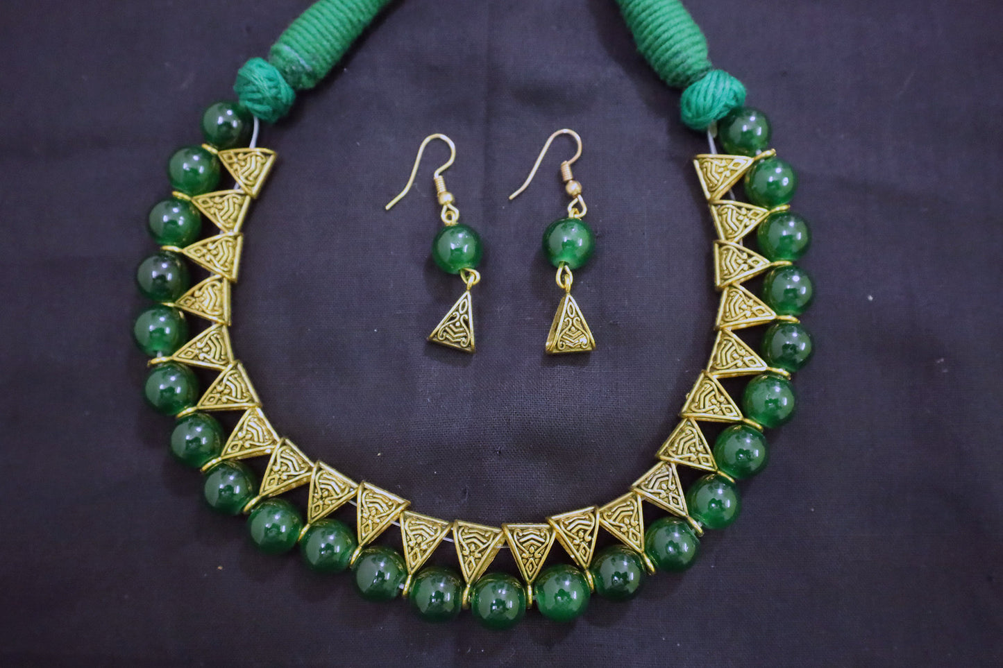 Bottom view of green glass beads golden loop necklace and earrings on black fabric