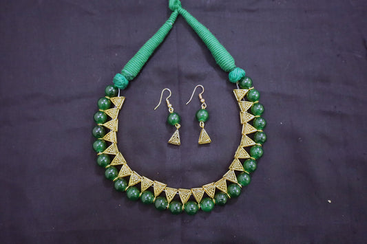 Top view of green glass beads golden loop necklace with earrings on black fabric