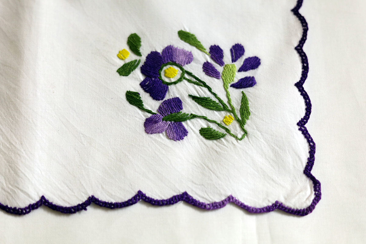 Close-up view of the hand embroidered violet and green designs on cotton napkins