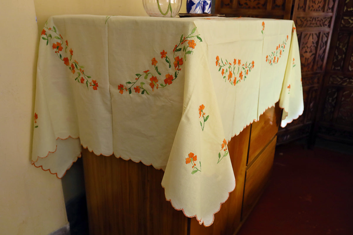 Side angle shot of Bright Orange Hand Embroidery Table Cloth showcasing its handmade designs with a chest of drawers.