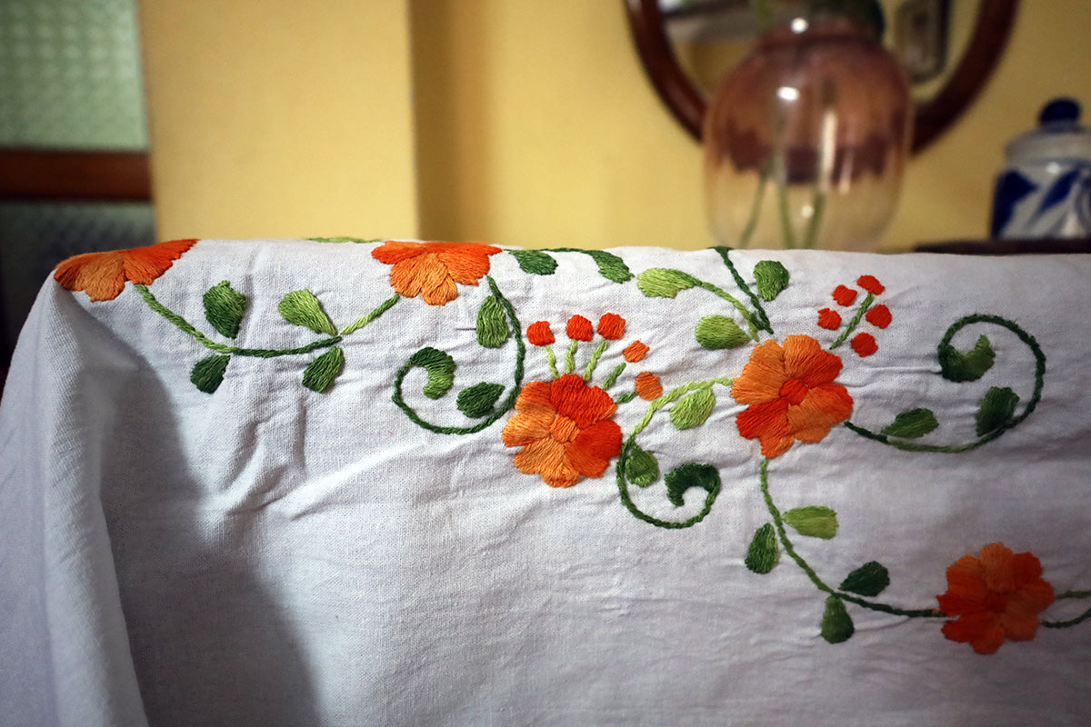 Close-up of Orange Hand Embroidery Table Cloth with intricate embroidery details beside a chest of drawers.