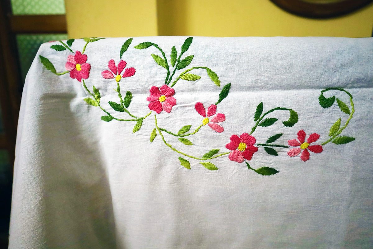 Close-up of Pink Hand Embroidery Table Cloth embroidery details and vibrant colors next to a chest of drawers.