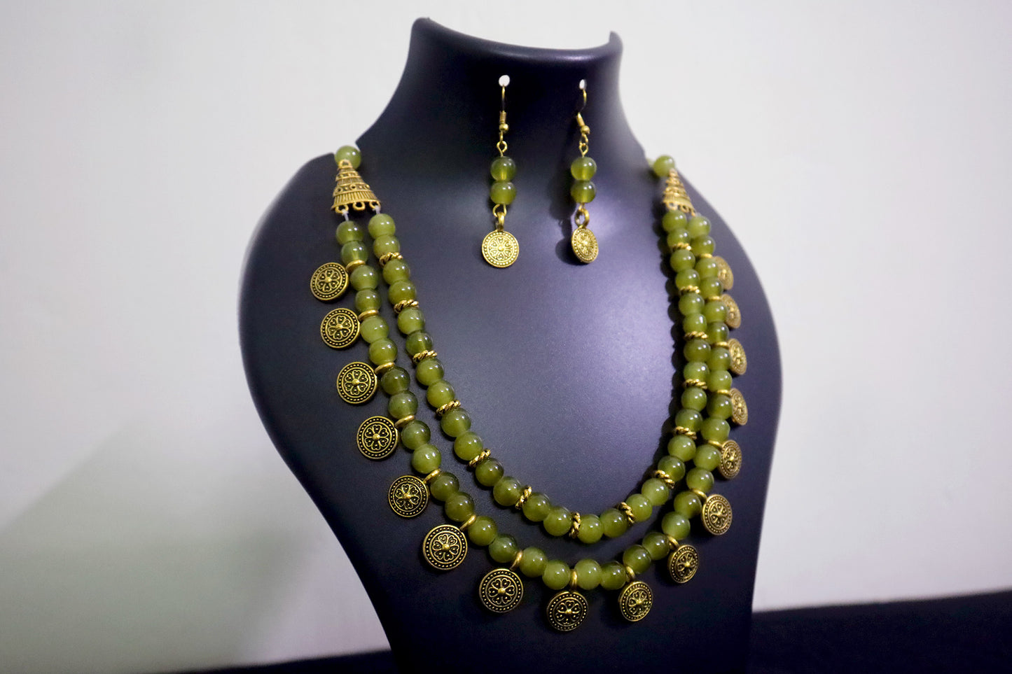 Closer view of light moss green glass beads golden ginni necklace set with earrings on black mannequin