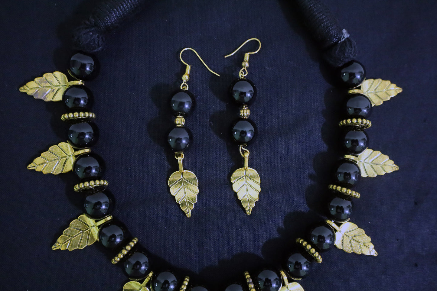 Middle section of handmade black beads necklace showing golden leaf charm and doughnut detailing.