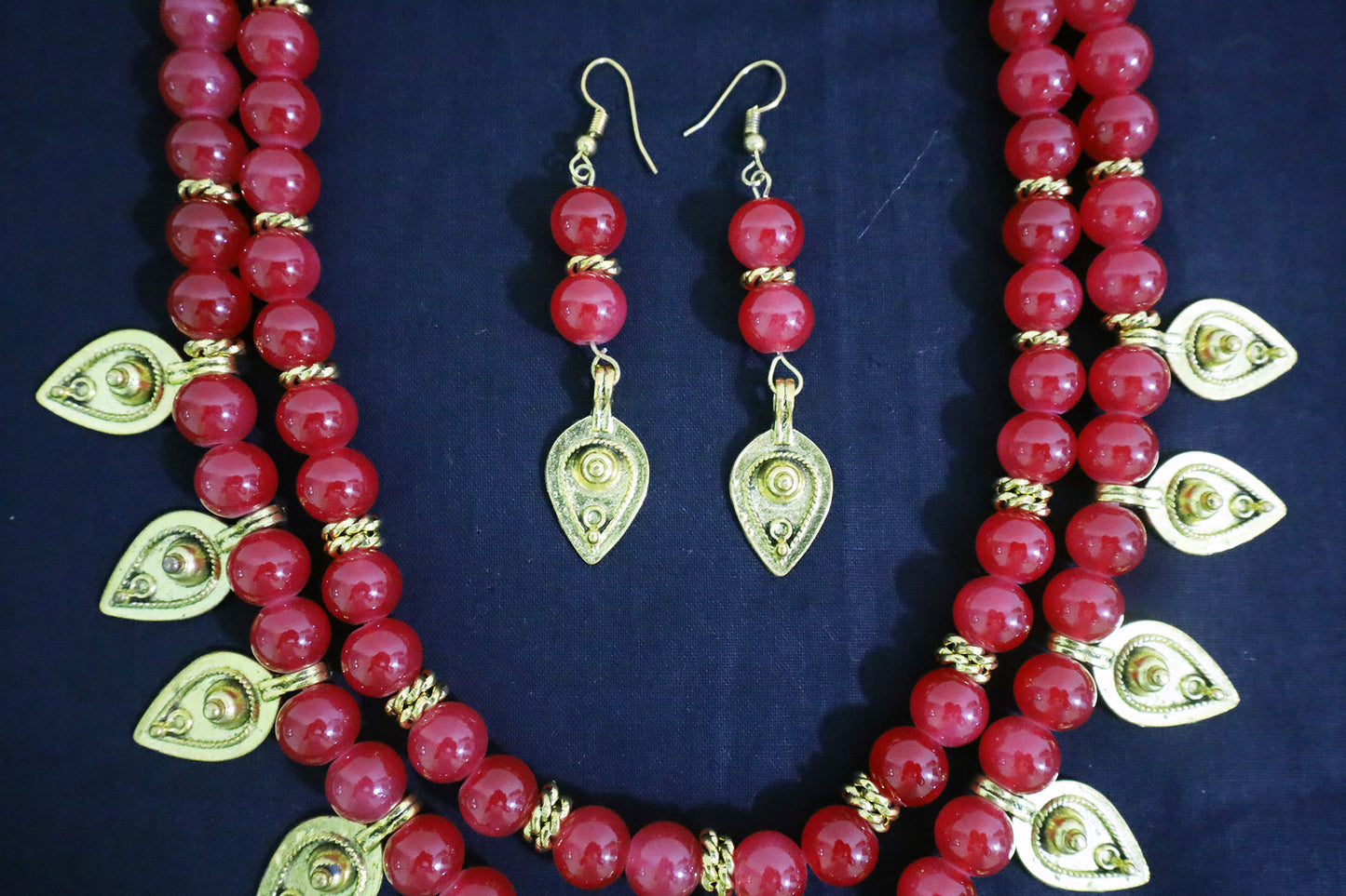 Middle view of red handmade necklace showing golden drop charm and glass bead detailing.