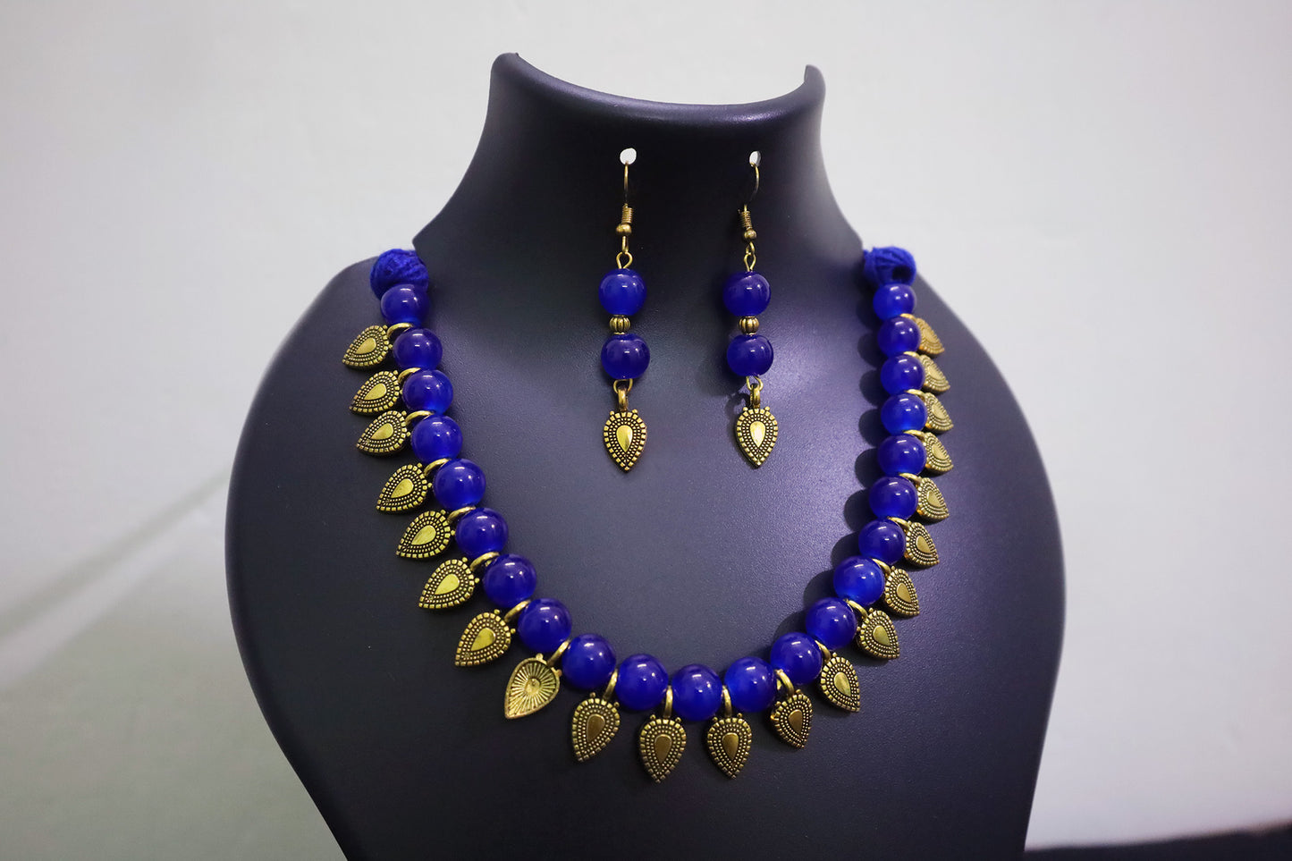 Navy blue glass beaded with golden leaf charm necklace and earrings set on a black mannequin bust against a white background