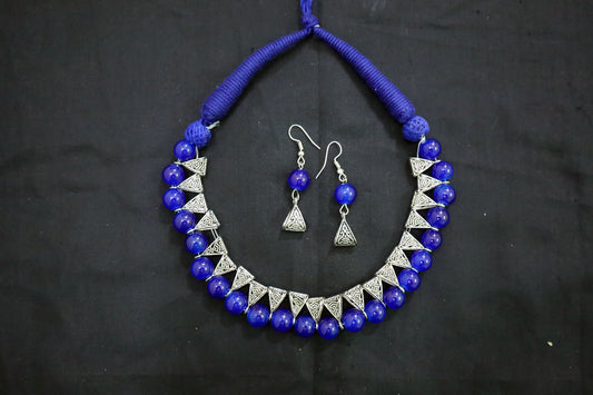 Top view of navy blue glass beads and earrings silver loop necklace on black fabric