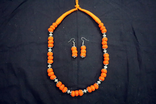 Top view of orange oxidized and cotton balls long necklace set on black background