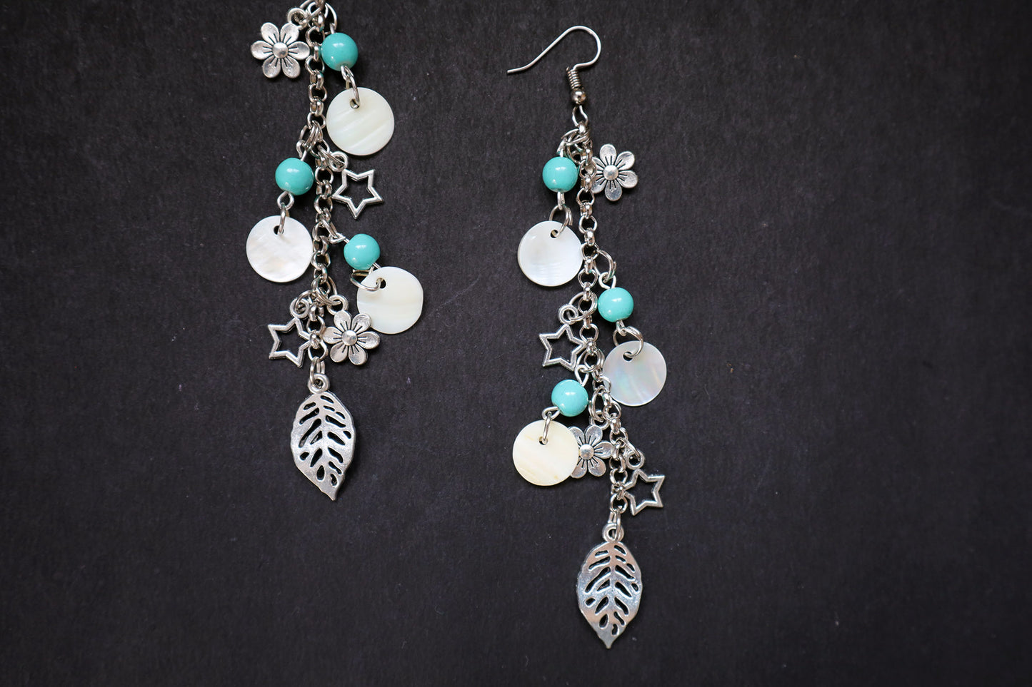 Closer view of pair of silver earrings with turquoise beads and leaf charms on a black background