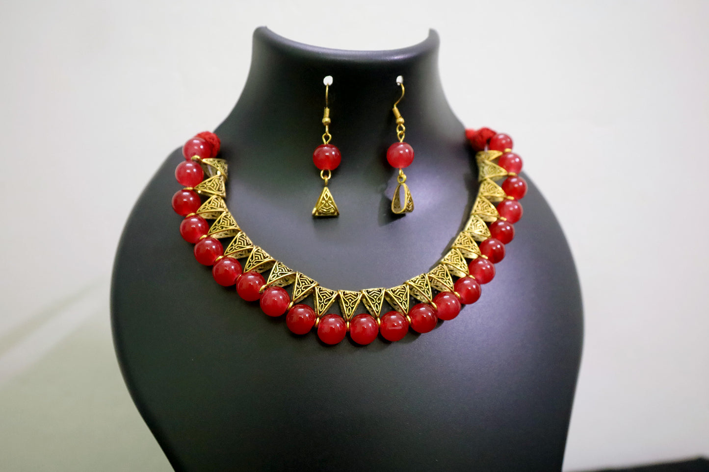 Closer view of red glass beads golden loop necklace set on black mannequin