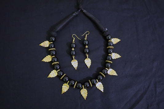 Top view of big black beads, golden leaf and doughnut necklace with matching earrings set.