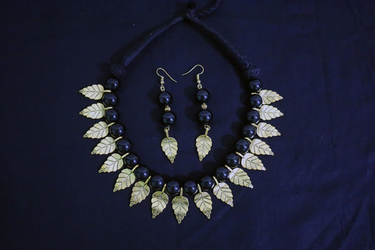 Top view of black glass beads and golden leaf charm necklace with earrings set on a black background.