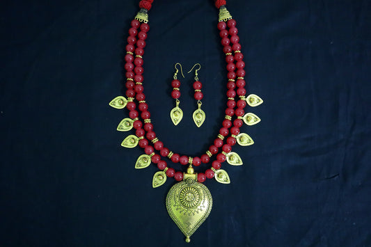 Top view of red glass beads and golden drop pendant necklace and earrings on black fabric.