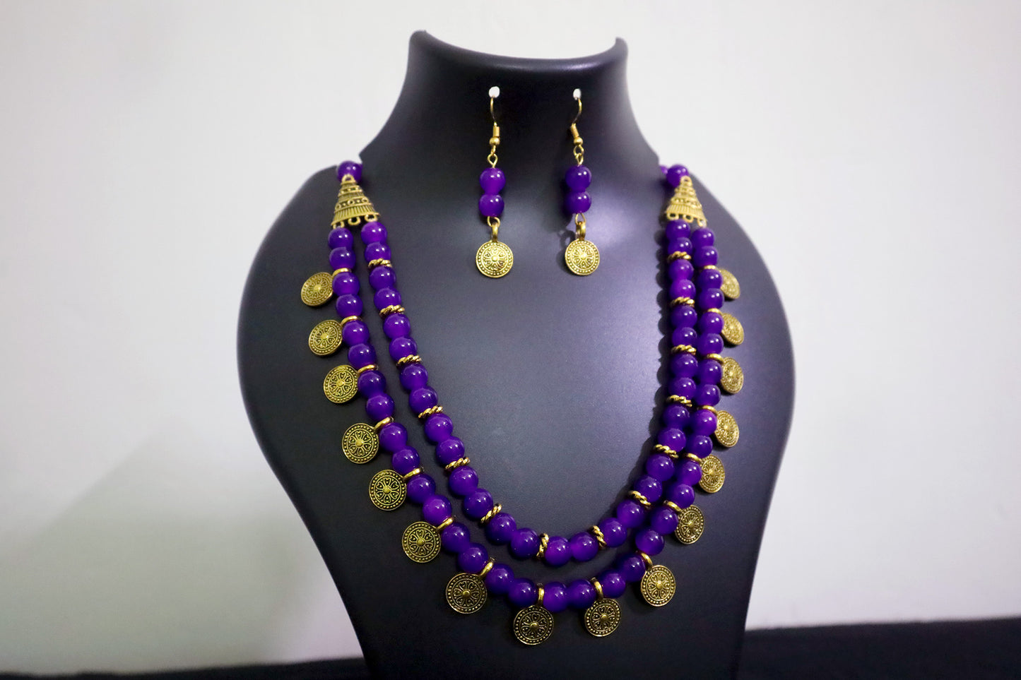 Closer view of violet 2 layered glass beads golden ginni necklace and earrings on black mannequin