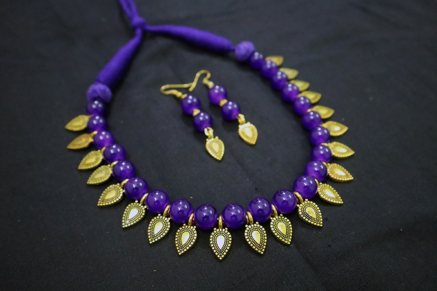 Violet beaded necklace with gold leaf accents and matching earrings on a dark background - handmade jewellery design