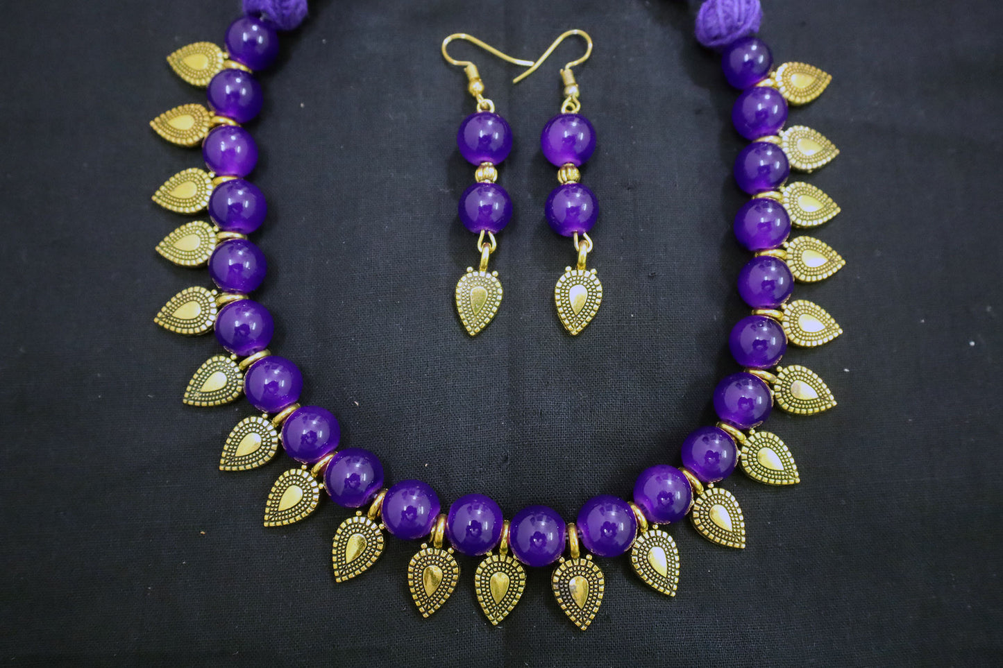 Violet beaded necklace with gold leaf and earrings on a black background - fashion jewellery online