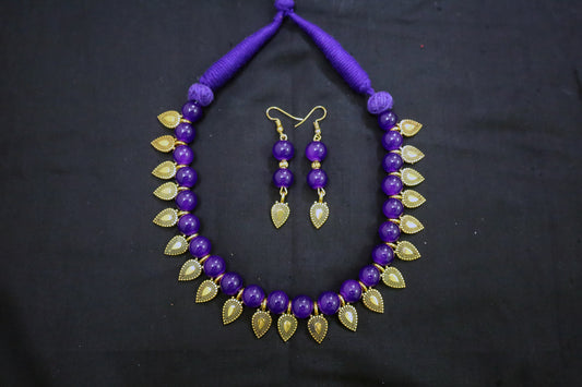 Violet beaded necklace with gold leaf accents and matching earrings on a black background - artificial jewellery online