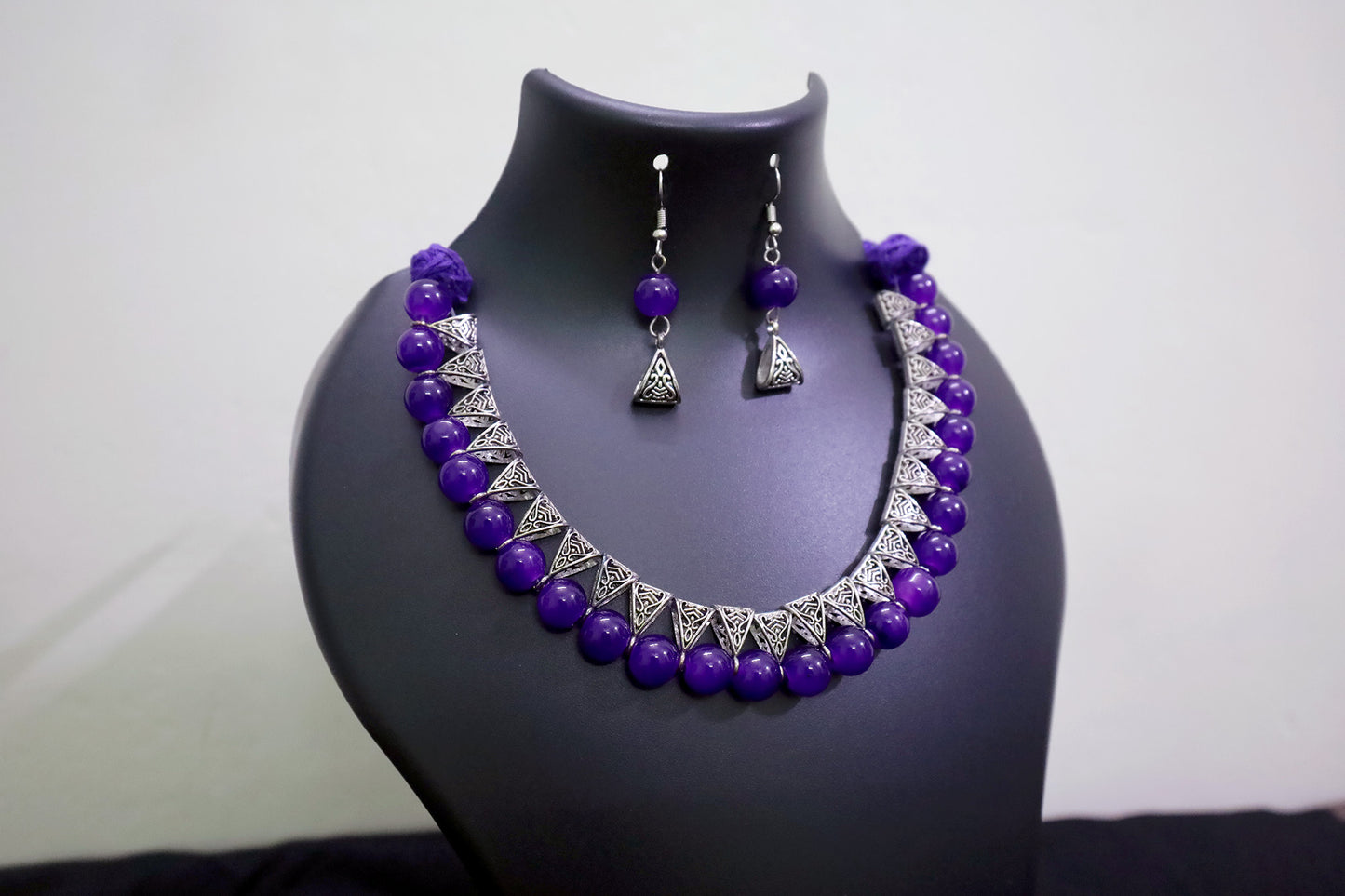 Closer view of violet glass beads silver loop necklace and earrings set on black mannequin