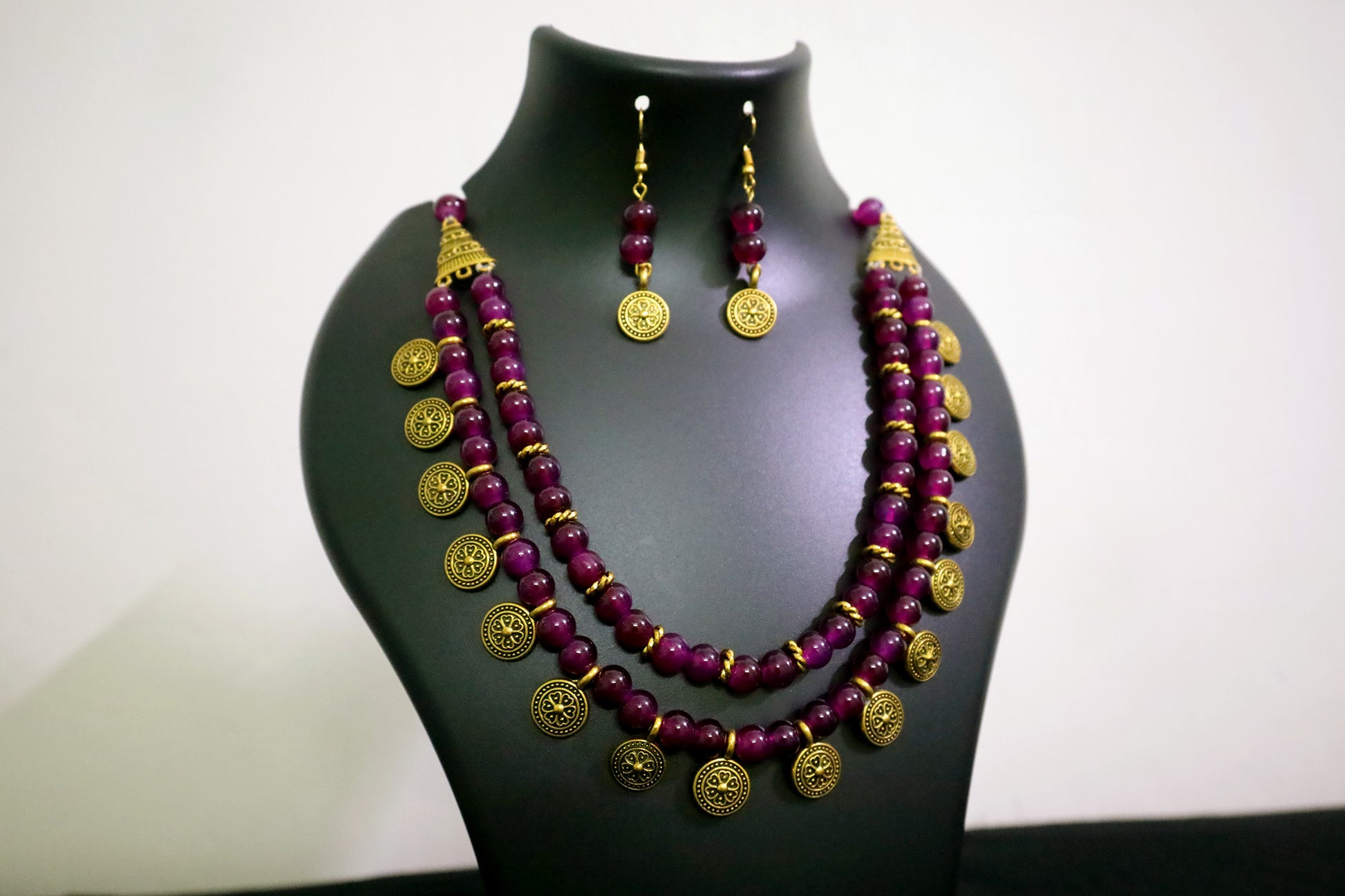 Closer view of amethyst 2 layered glass beads and golden ginni necklace with earrings on black mannequin