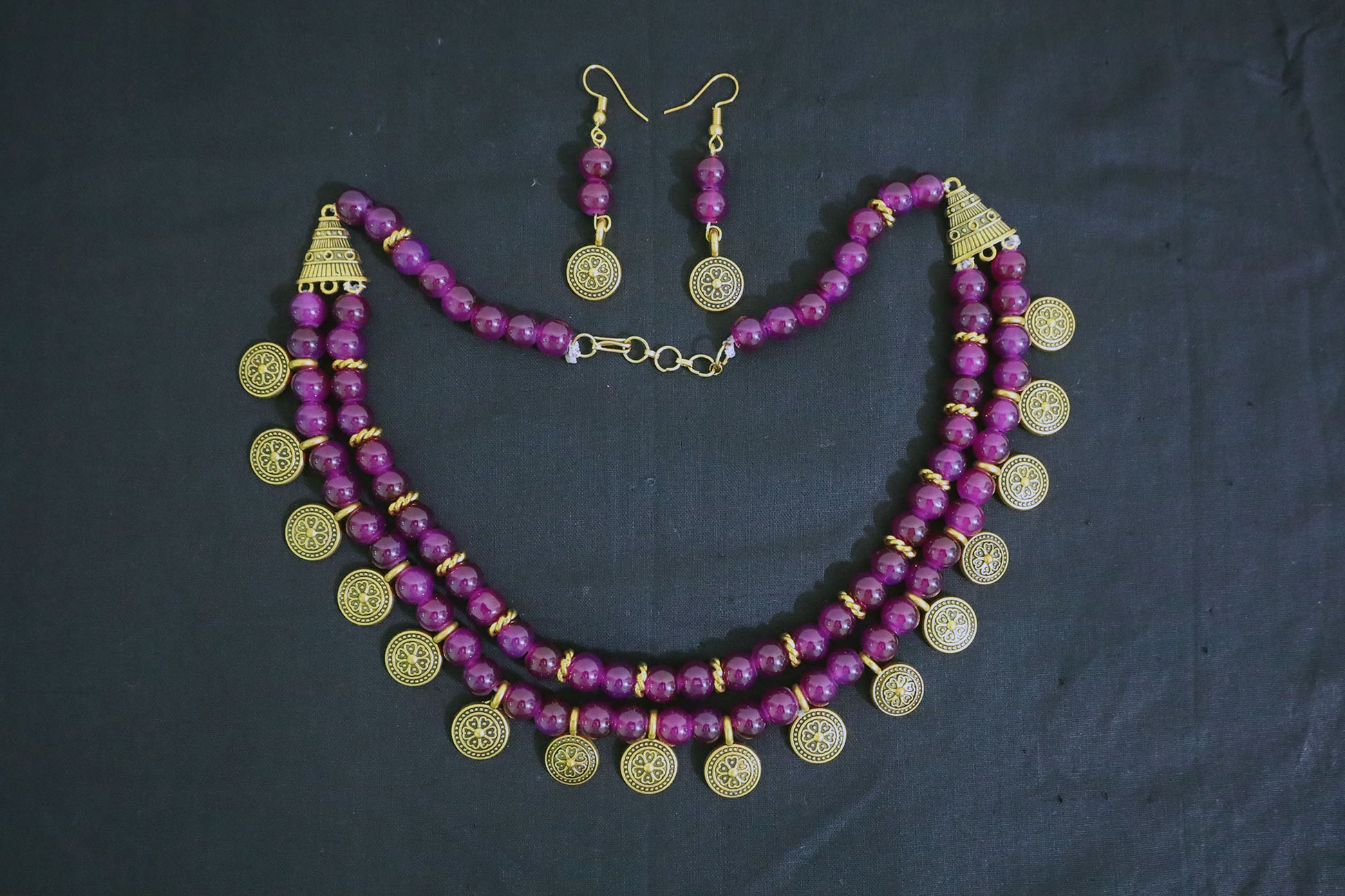 Top view of amethyst glass beads and golden ginni necklace with earrings on black fabric