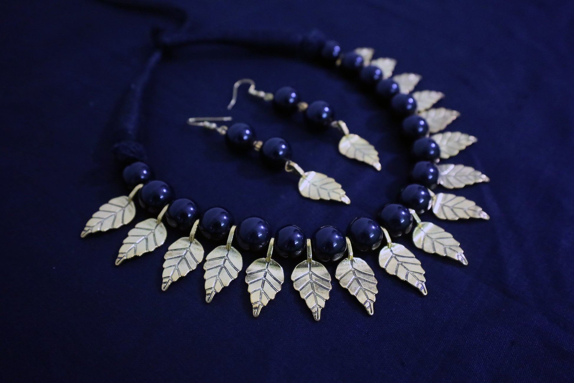 Angle view of handmade black glass beads and golden leaf charm necklace with matching earrings.