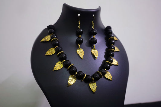 Closer view of handmade black beads and golden leaf charm necklace with earrings on a black mannequin.