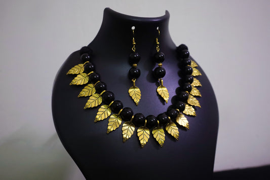 Closer view of black glass beads and golden leaf charm necklace with earrings displayed on a black jewellery mannequin.
