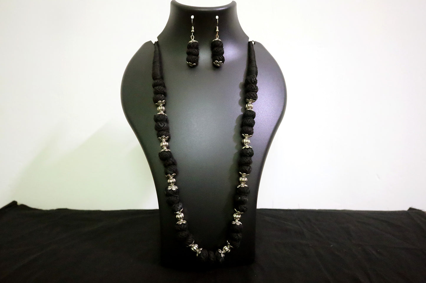 Closer view of black oxidized balls and cotton balls long necklace with earrings on mannequin.
