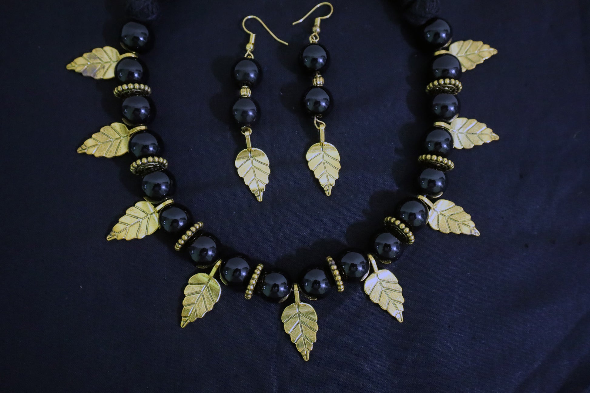 Bottom close-up of big black glass beads necklace and earrings with golden leaf and doughnut design.
