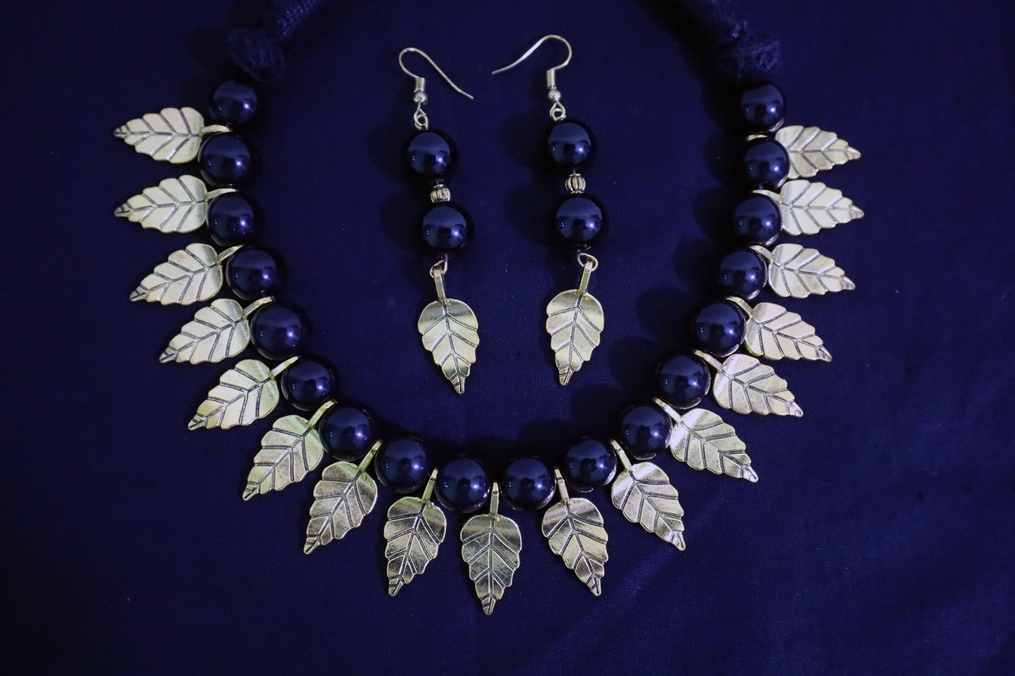 Bottom close-up of black glass beads necklace and earrings set with golden leaf charms.