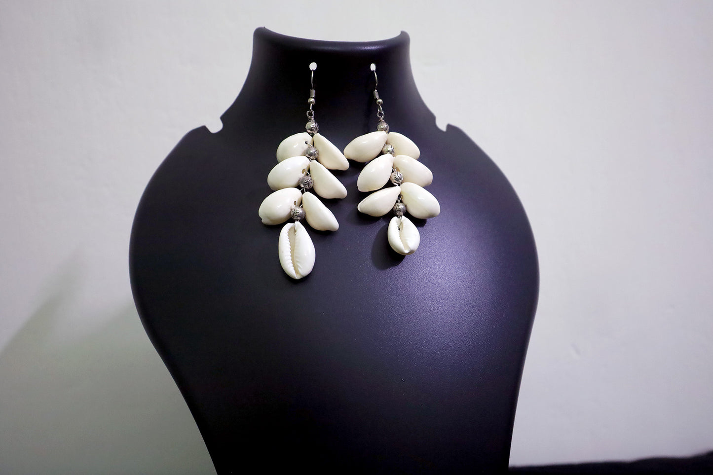 Close-up of handcrafted pair of Cowrie Seashell & Metal Ball Dangle Earrings on black mannequin