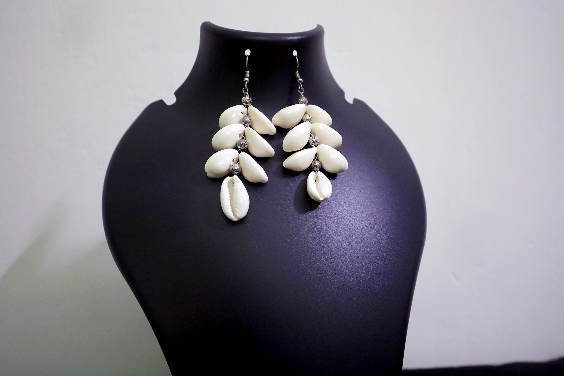 Close-up of handcrafted pair of Cowrie Seashell & Metal Ball Dangle Earrings on black mannequin