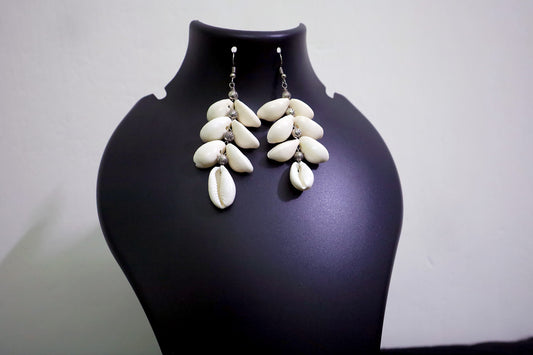 Close-up of handcrafted pair of Cowrie Seashell & Metal Ball Dangle Earrings on black mannequin