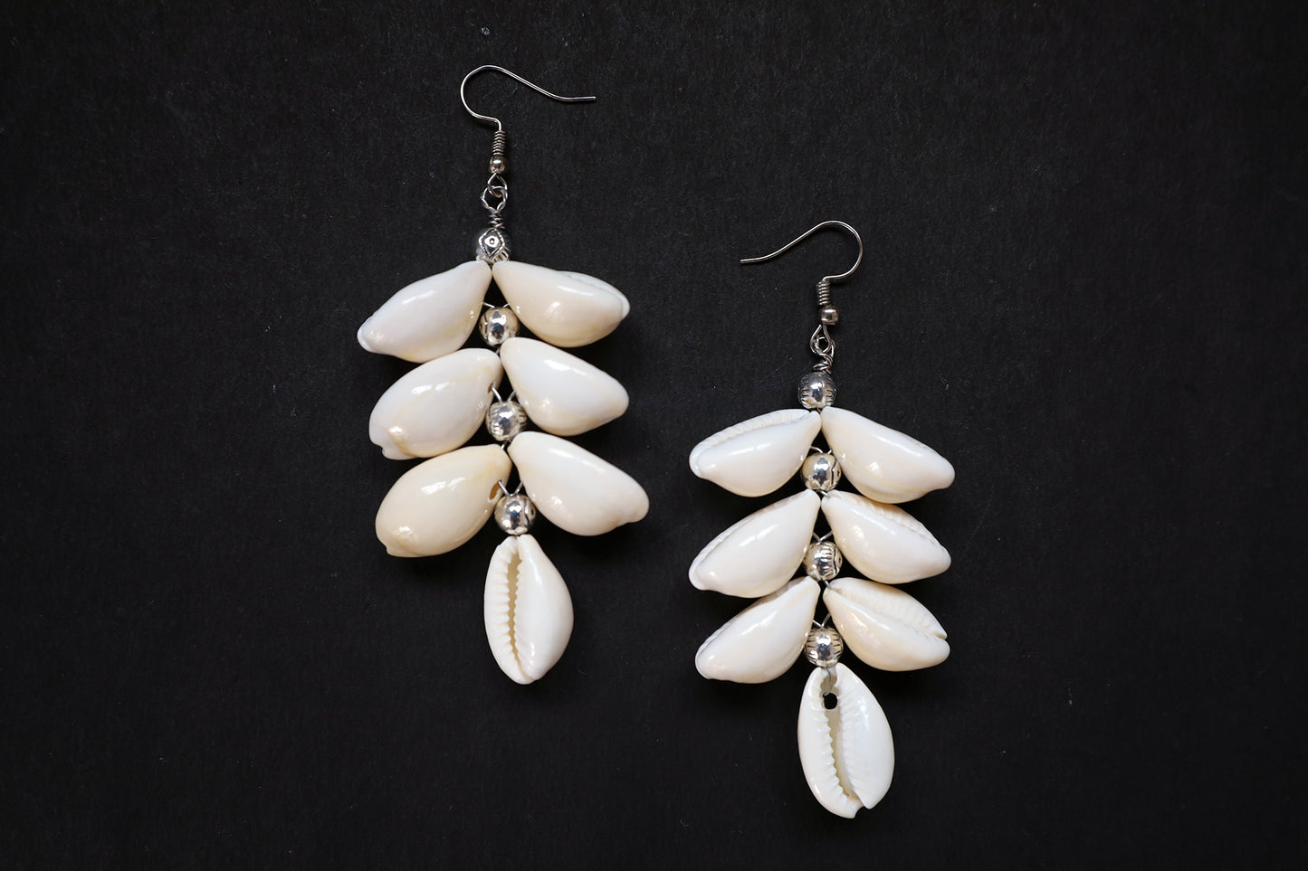 Top view of pair of Cowrie Seashell & Metal Ball Dangle Earrings on black fabric background
