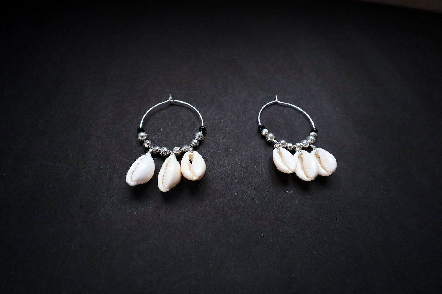 Angled view of pair of oxidized Cowrie Seashell & Metal Ball Hoop Earrings showcasing intricate design
