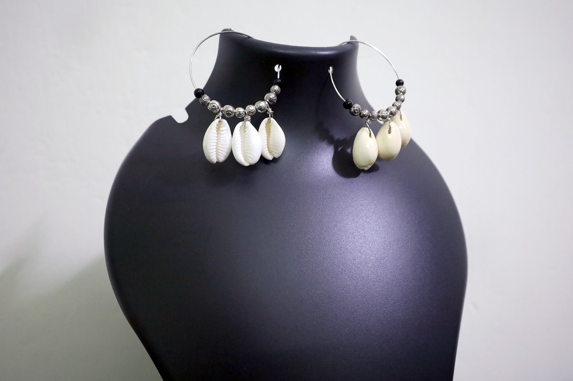 Close-up view of pair of Cowrie Seashell & Metal Ball Medium Hoop Earrings on black mannequin