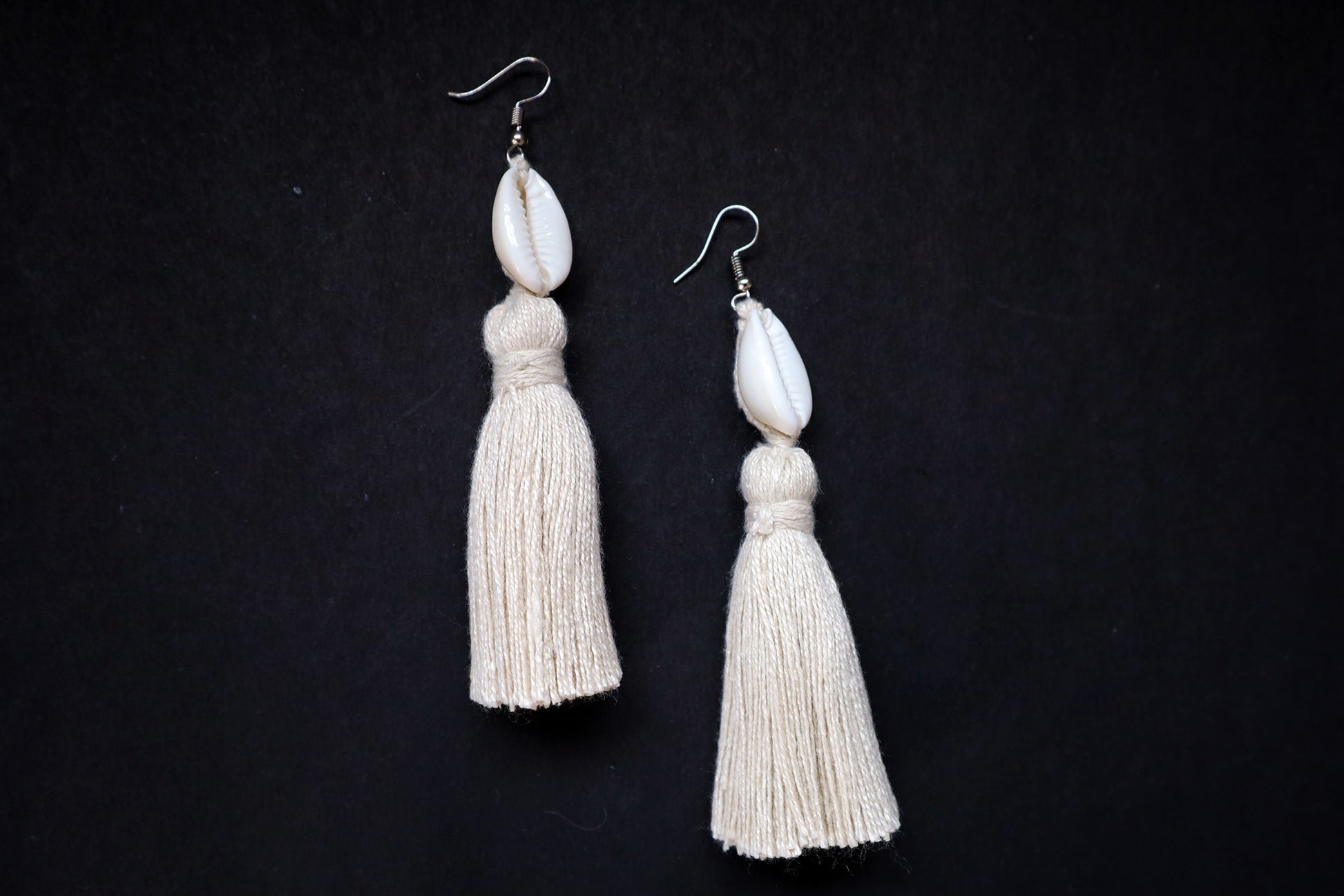 Top view of Cowrie Seashell & Off-white Tussle Dangle Earrings on black fabric background