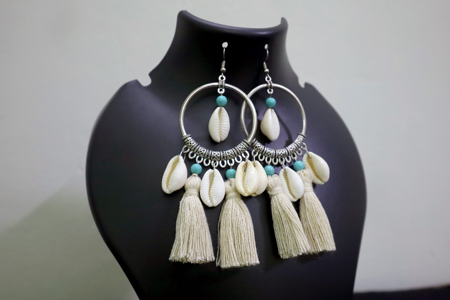 Closer view of pair of cowrie seashell and tussle oxidized hoop dangle earrings on black mannequin