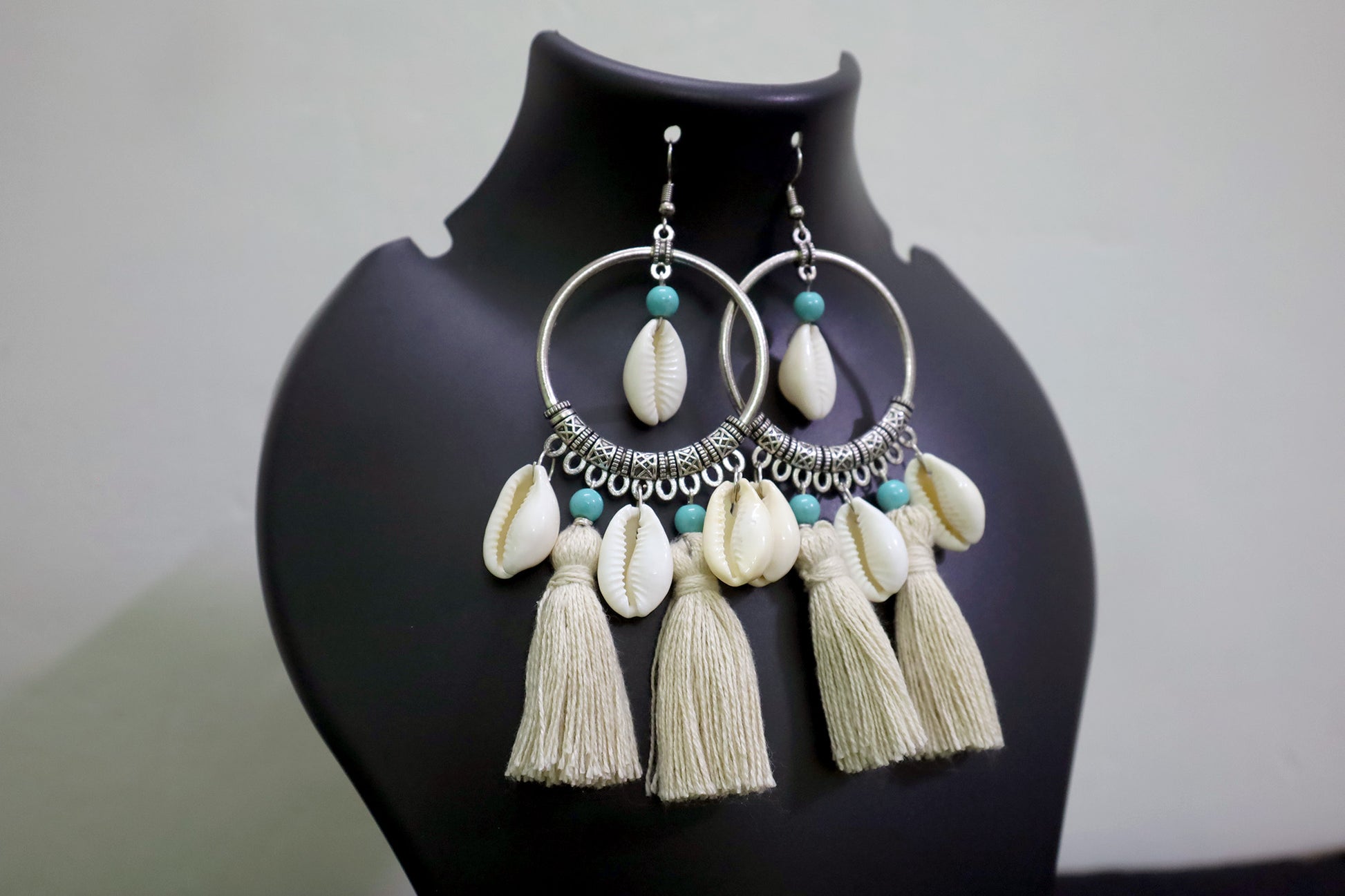 Closer view of pair of cowrie seashell and tussle oxidized hoop dangle earrings on black mannequin