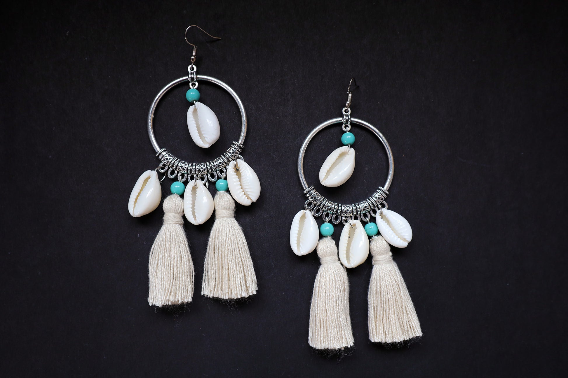Top view of handcrafted pair of cowrie seashell and tussle oxidized hoop dangle earrings