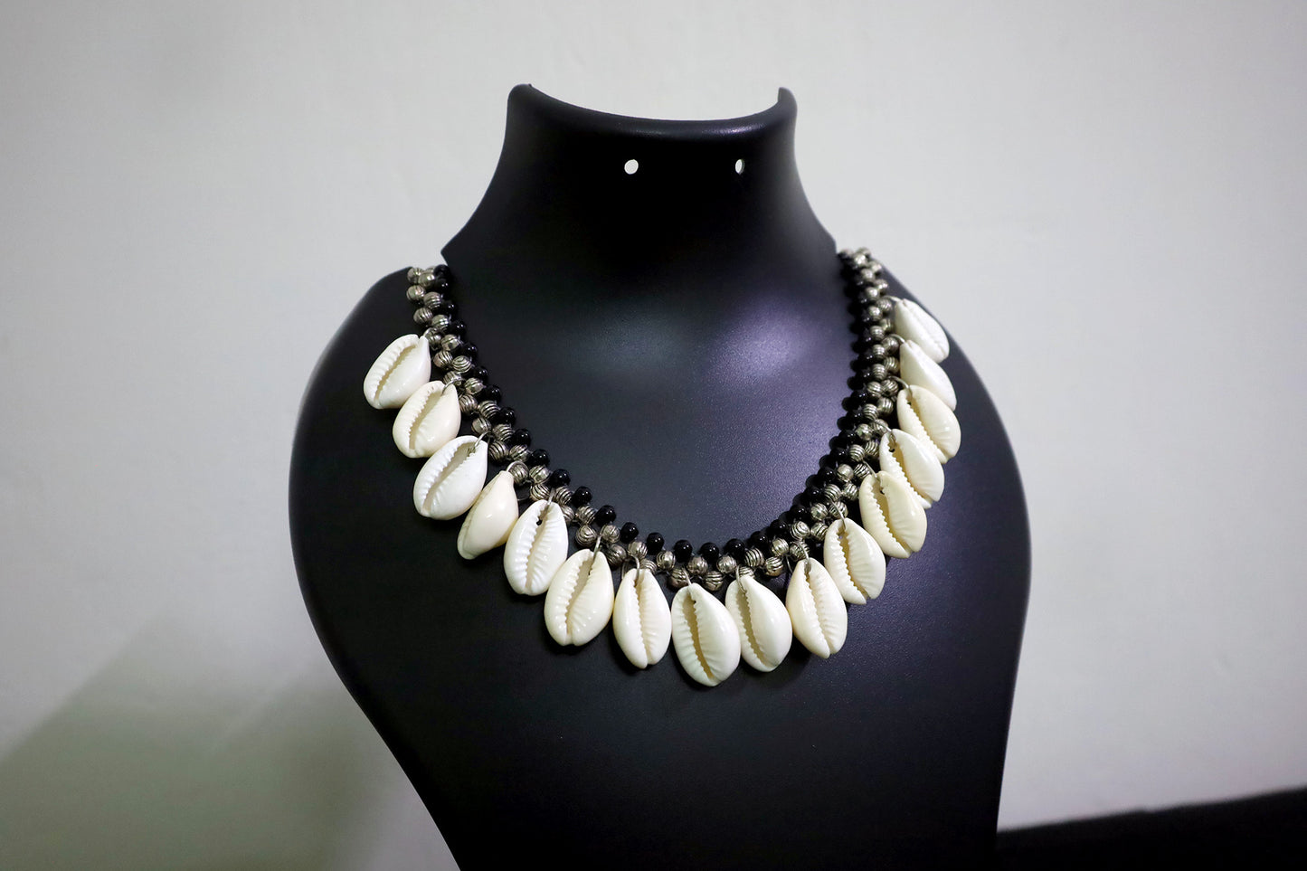Closer view of short metal beads and cowrie silver colored necklace on black mannequin.