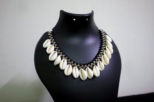 Closer view of short metal beads and cowrie silver colored necklace on black mannequin.