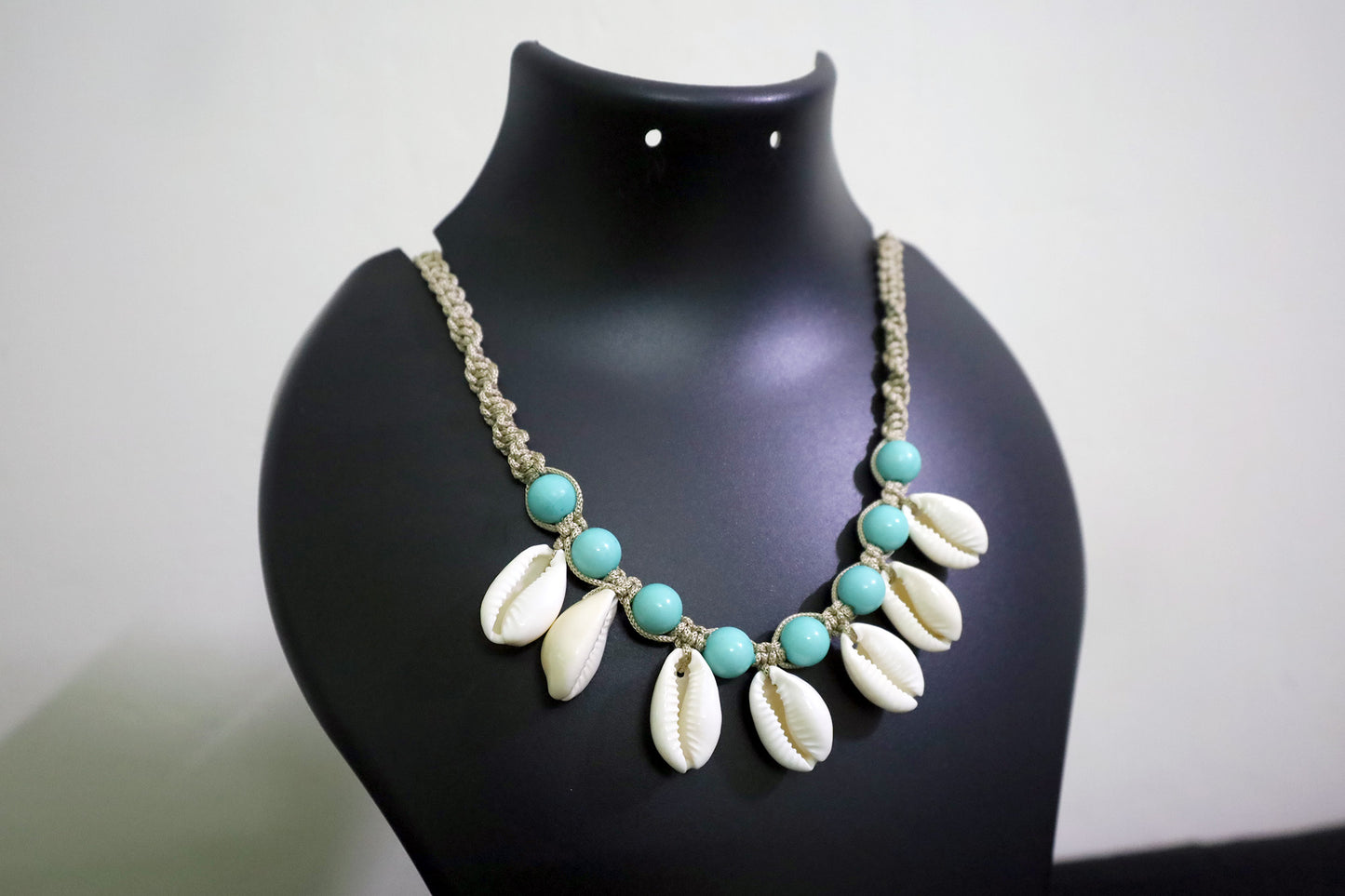 Necklace with turquoise beads and white shell-like pendants on a black mannequin.